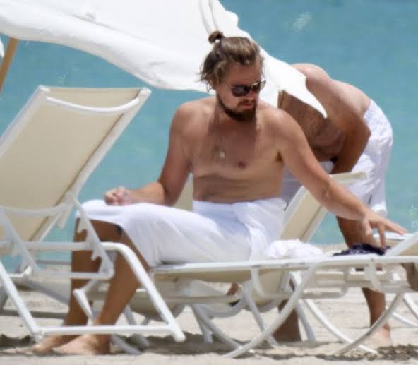 A bearded man reclining poolside in a paparazzi-style shot — allegedly the star, mid-snack.